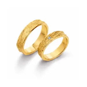 Zwei goldene Eheringe mit gehämmertem Finish, einer mit einem kleinen Diamanten. Perfekt für Hochzeit oder Jubiläum.