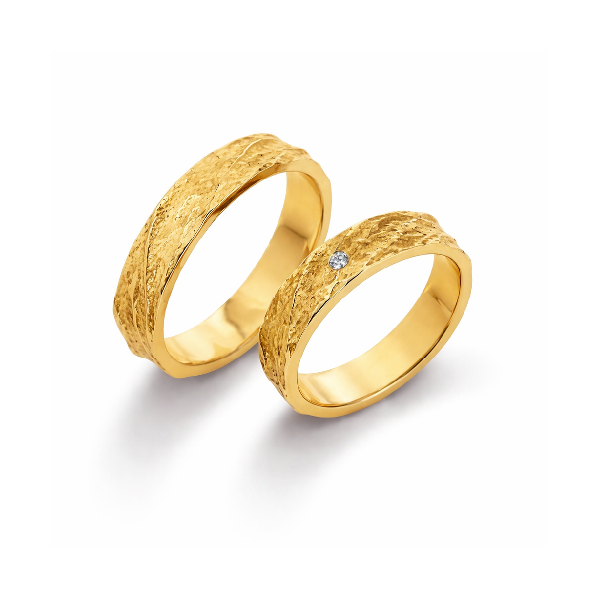 Zwei goldene Eheringe mit gehämmertem Finish, einer mit einem kleinen Diamanten. Perfekt für Hochzeit oder Jubiläum.