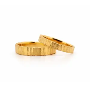 Zwei goldene, rustikal strukturierte Eheringe auf weißem Hintergrund, symbolisieren ewige Liebe und Verbundenheit.