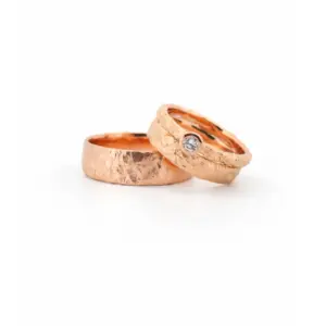 Zwei handgefertigte Eheringe aus Roségold, einer mit Diamant, auf weißem Hintergrund.