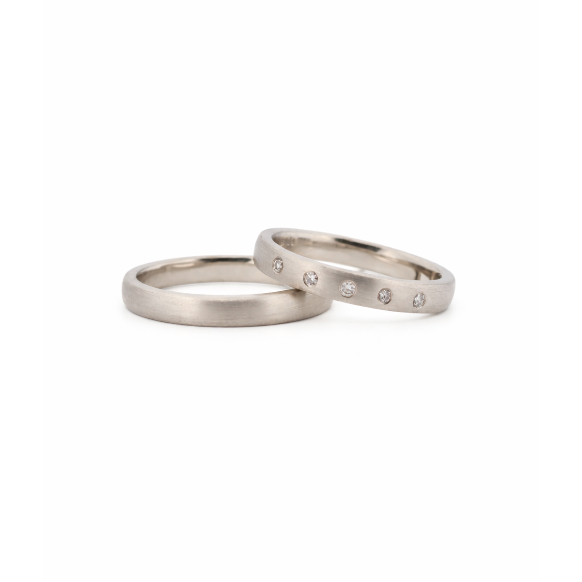 Zwei elegante Platin-Eheringe, einer schlicht, der andere mit Diamanten besetzt, vor weißem Hintergrund.
